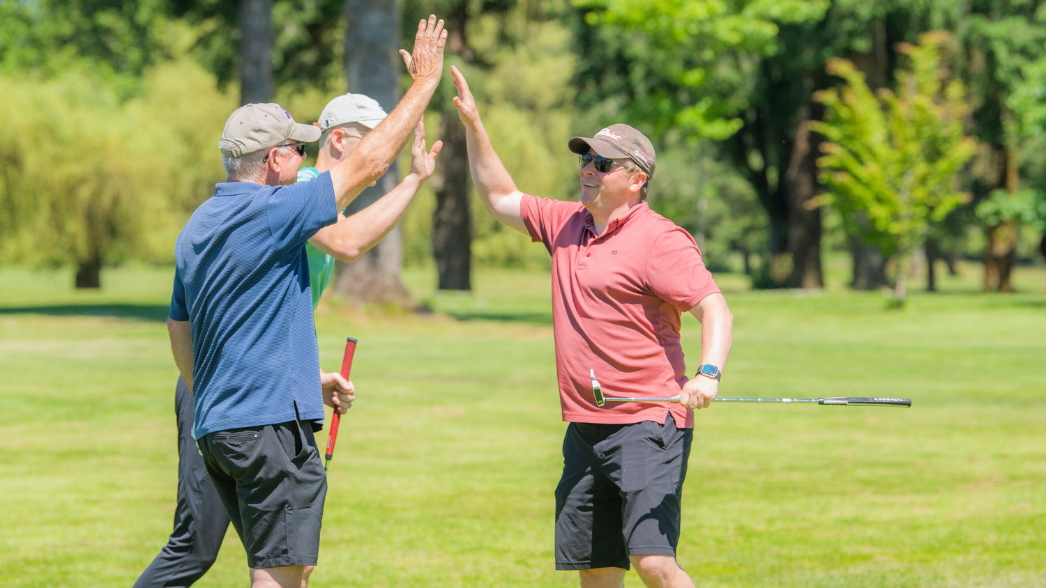 Ryan Stanbery sourit et tape dans les mains Mark McHugh et Craig Kline lors d'un tournoi de golf caritatif au Riverside Golf Course à Chehalis vendredi après avoir pris un put.